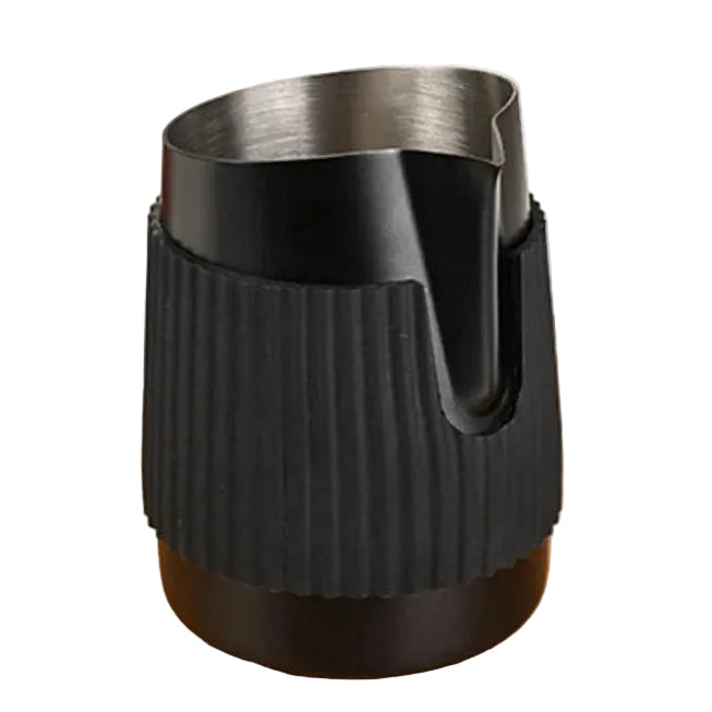A black insulated travel mug with a ribbed silicone sleeve and stainless steel rim, shown on a wooden tabletop with a glass carafe of tea blurred in the background.