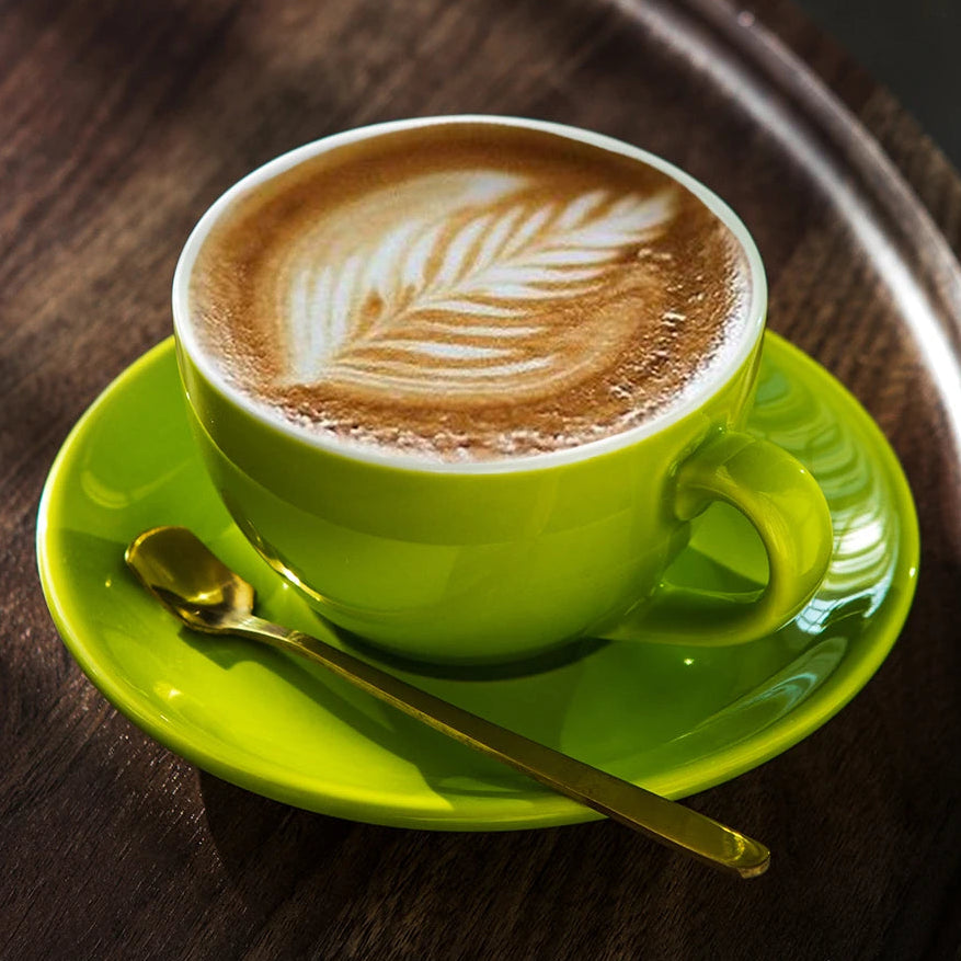 A bright lime green ceramic coffee cup filled with latte art sits on a matching saucer with a gold spoon, placed on a dark wooden tray.